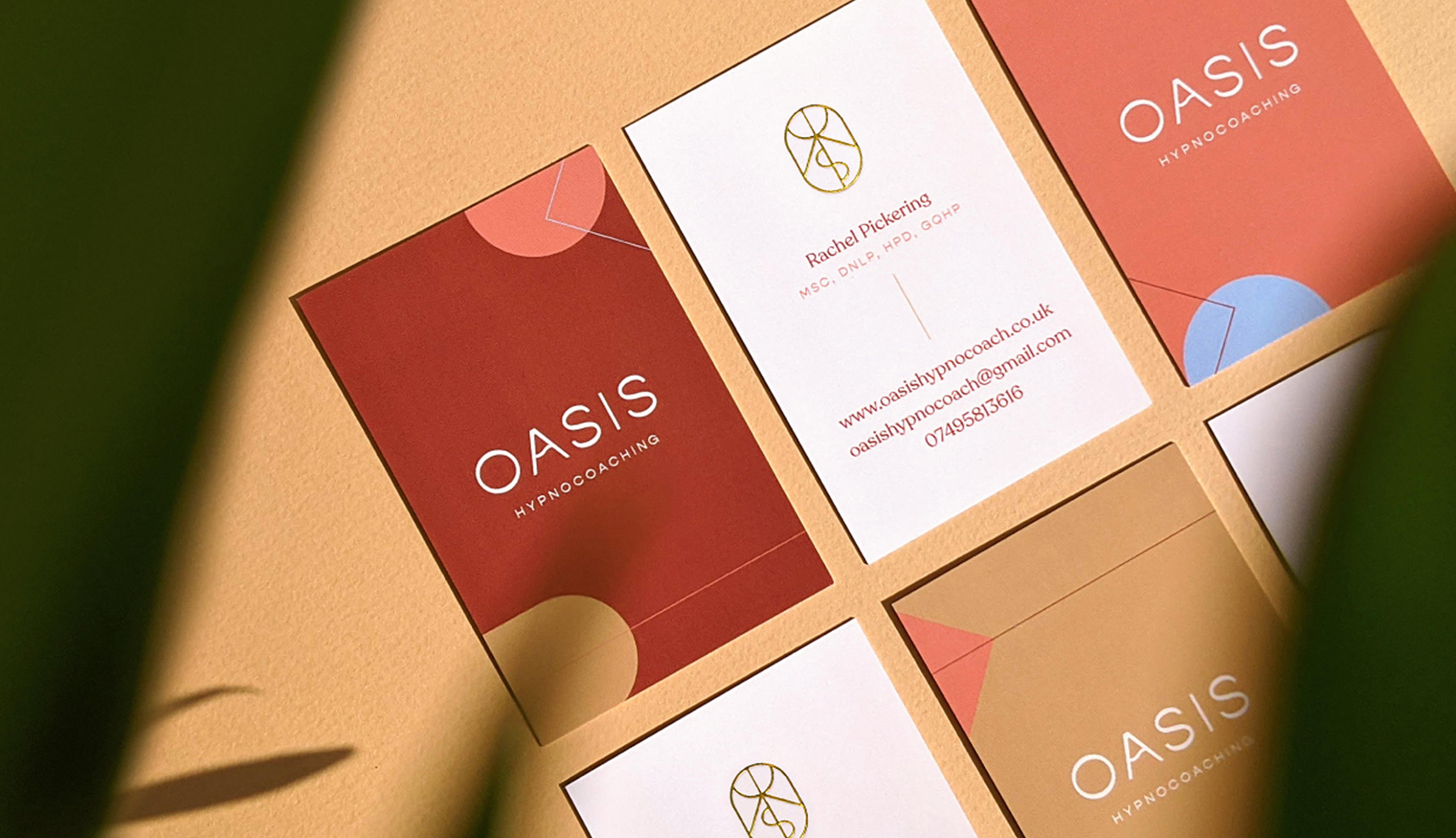 Oasis business cards in terracotta, cream and sand, laid out in sunlight with the gold logomark foiled on one