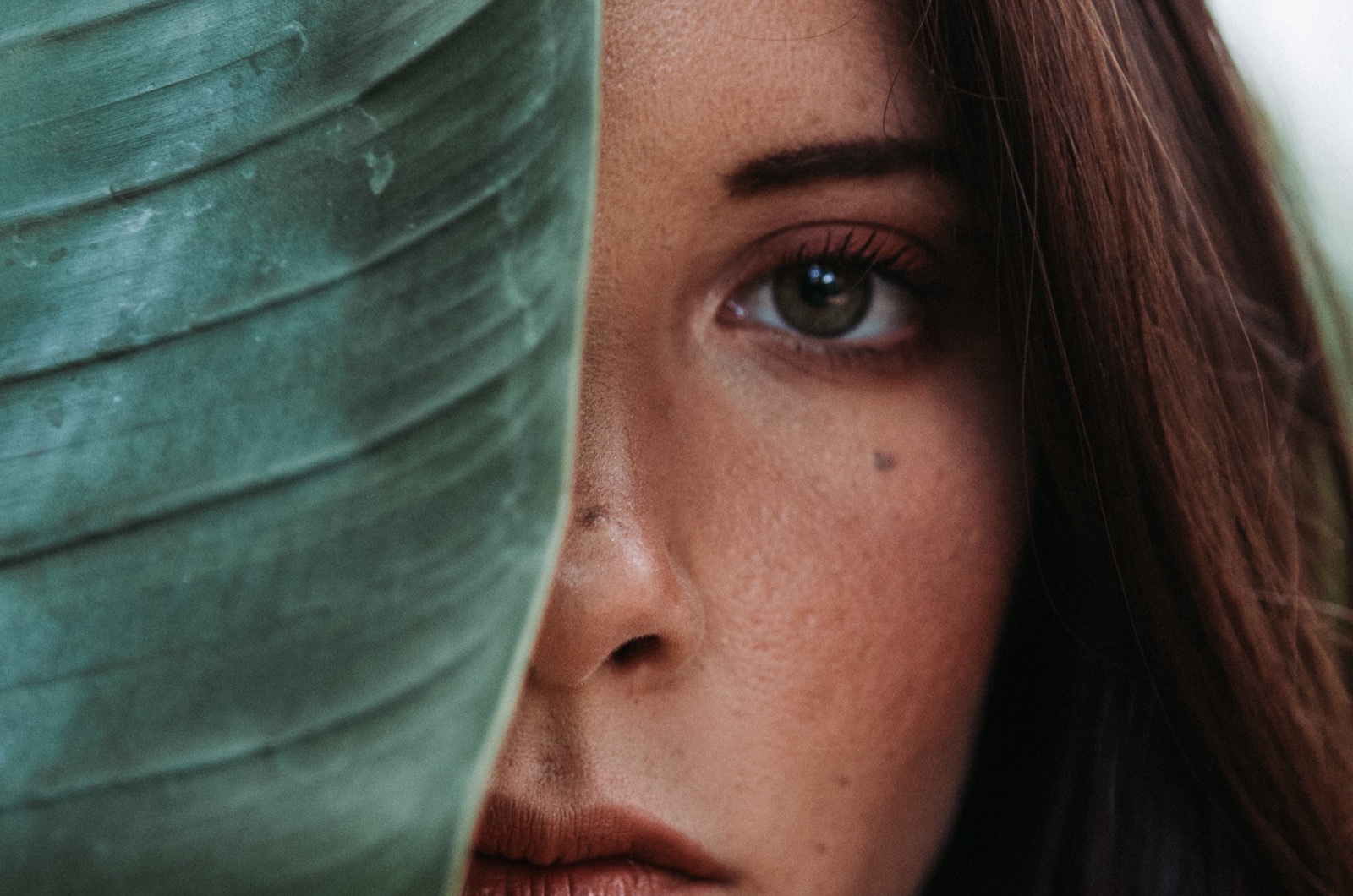 A woman's face half hidden behind a large leaf