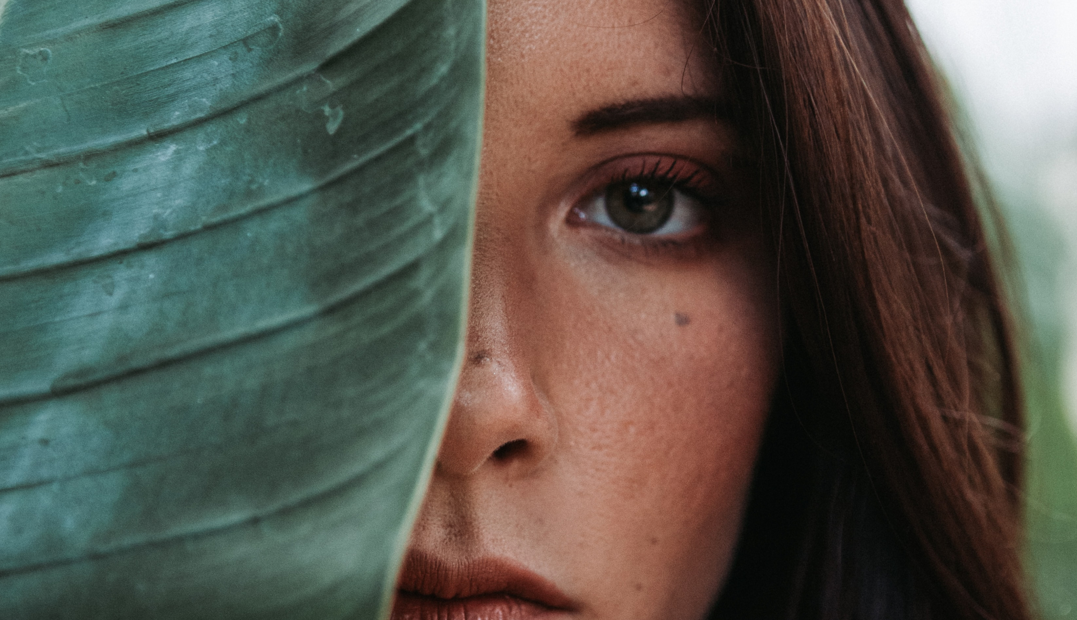 A woman's face half hidden behind a large leaf