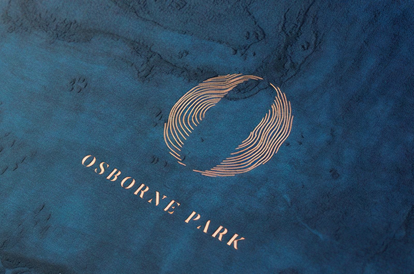 The Osborne Park mark and wordmark blocked in copper foil on deep blue textured board, the roundel drawn as two combed arcs