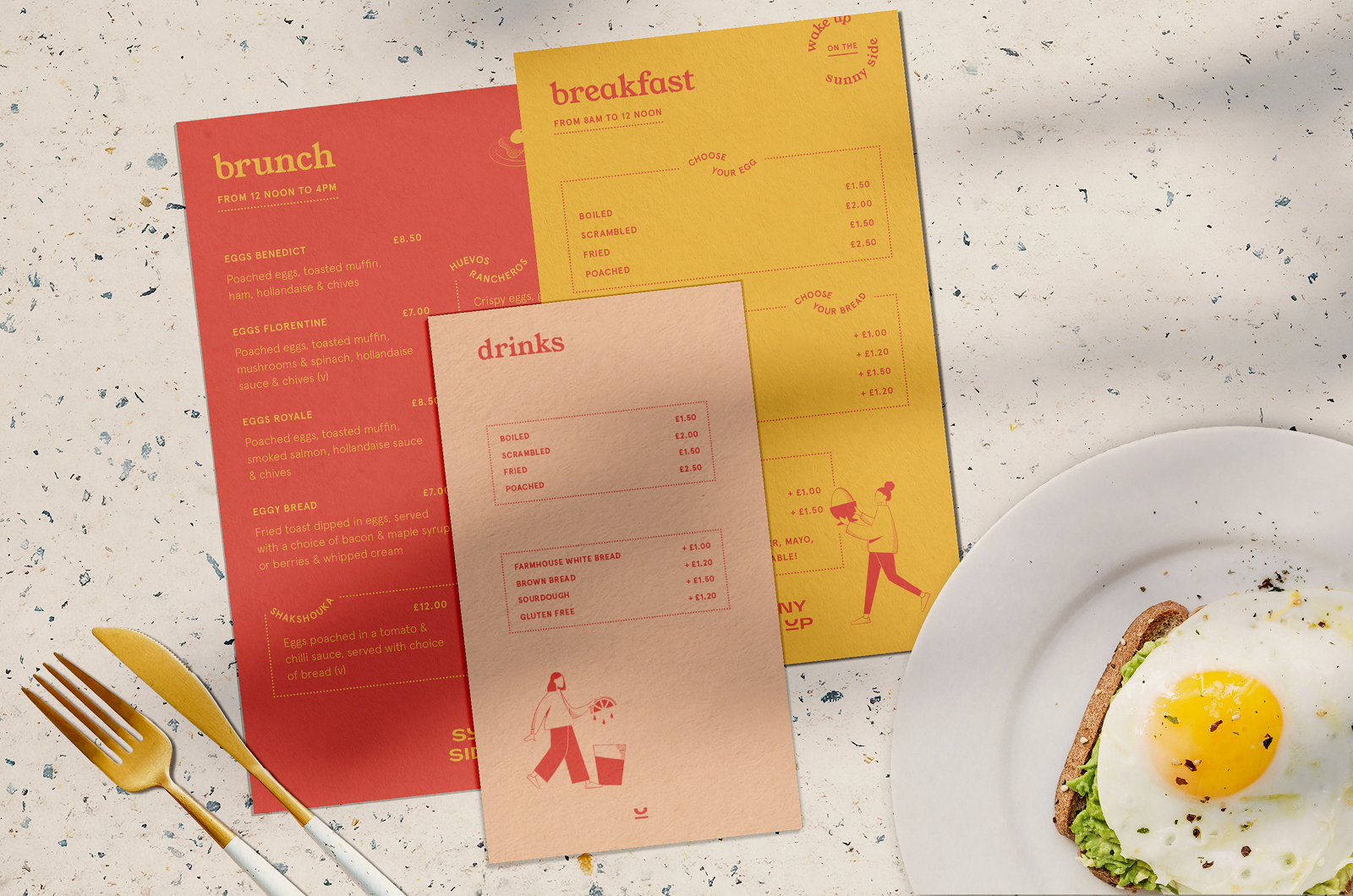 Sunny Side Up menus fanned out on a terrazzo table beside gold cutlery and a plate of avocado and fried egg on toast, the brunch card in red, breakfast in yellow and drinks in blush