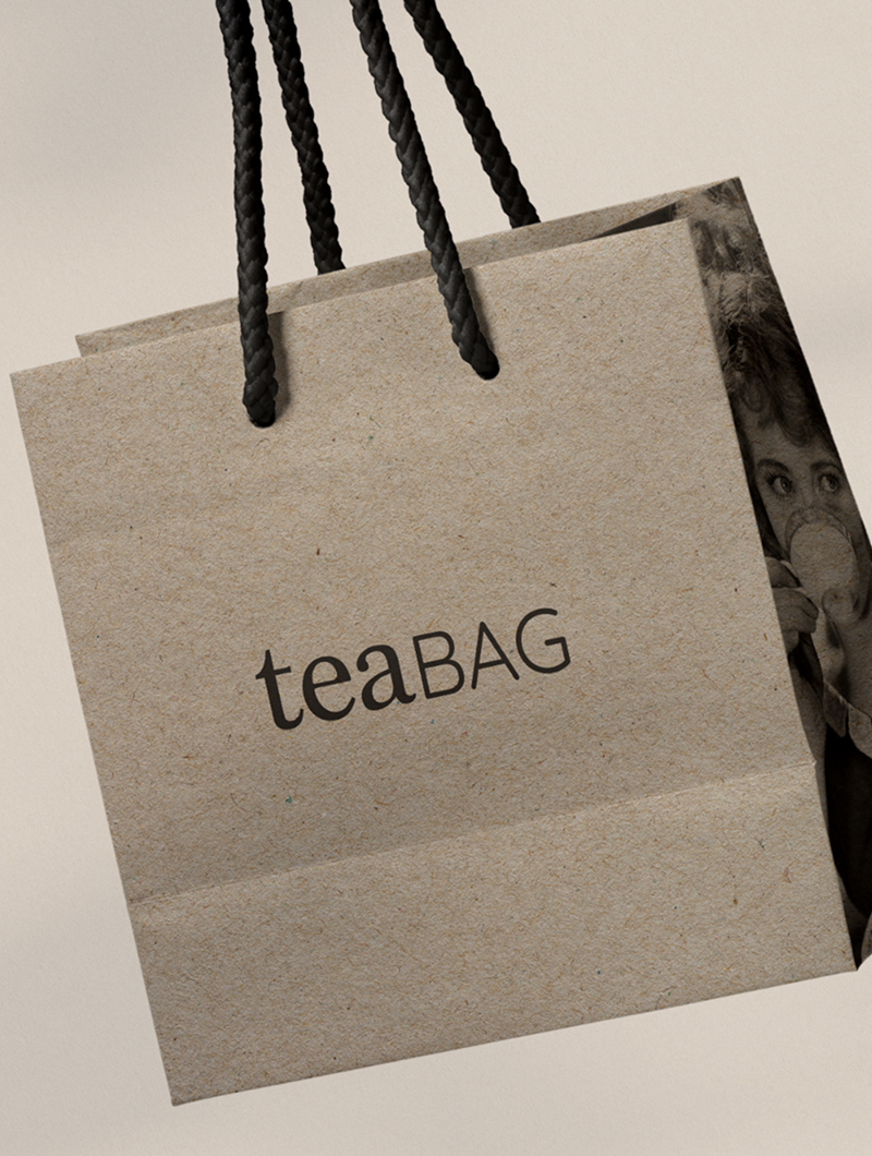A kraft paper carrier with rope handles printed teaBAG, a duotone photograph showing through its opening
