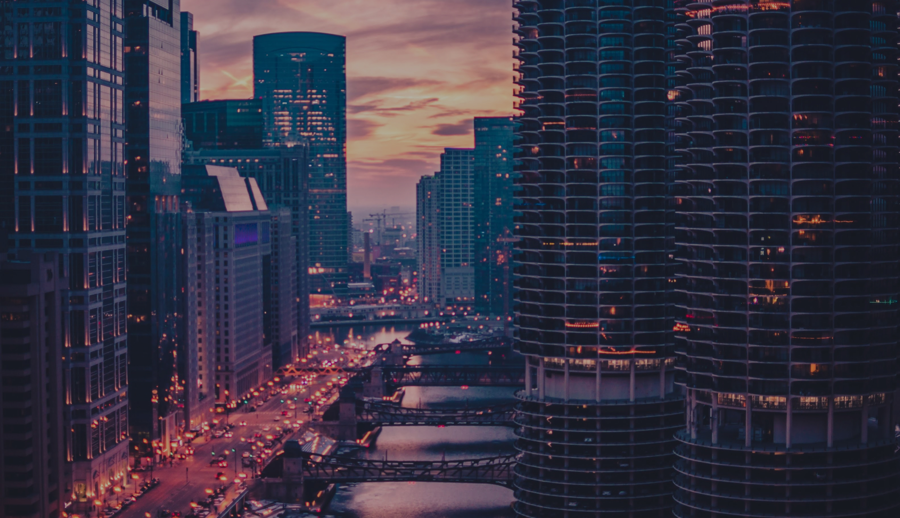 A city of high-rise towers at dusk, lit windows above a river