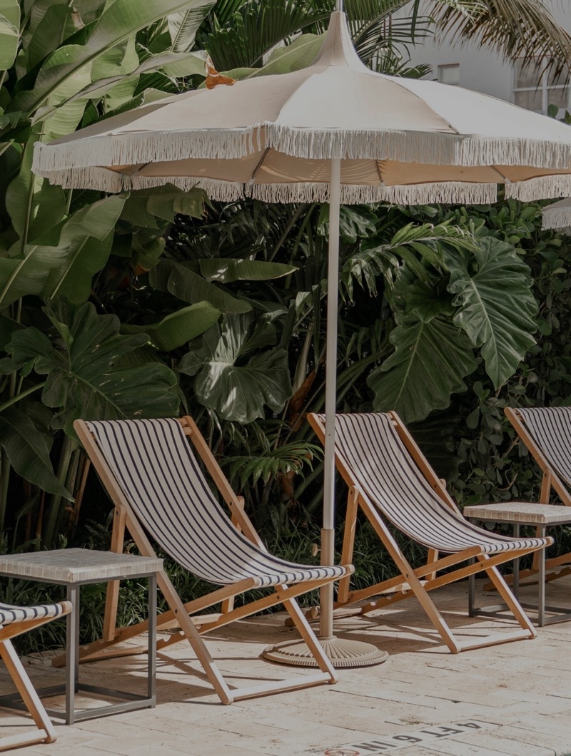 Striped deck chairs under fringed parasols beside a pool, backed by tropical planting
