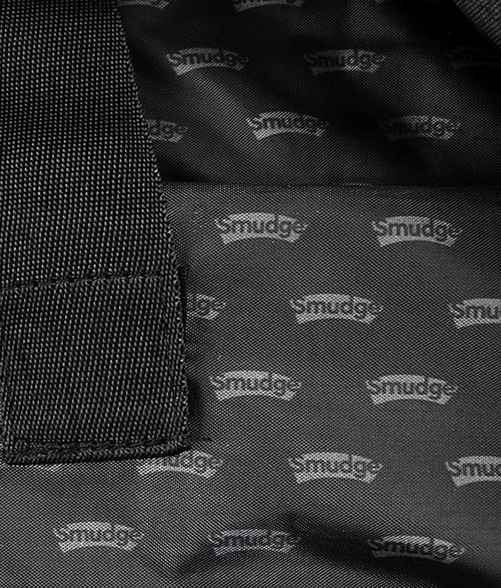 The backpack's black lining, woven all over with a small repeating Smudge wordmark, beside a webbing strap